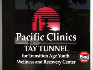 Pacific Clinics TAY Tunnel logo in white letter on black background with a red doorway. Pacific Clinics TAY TUNNEL for Transition Age Youth Wellness and Recovery Center logo.